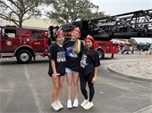 three girls with fire hats on in front of tower truck